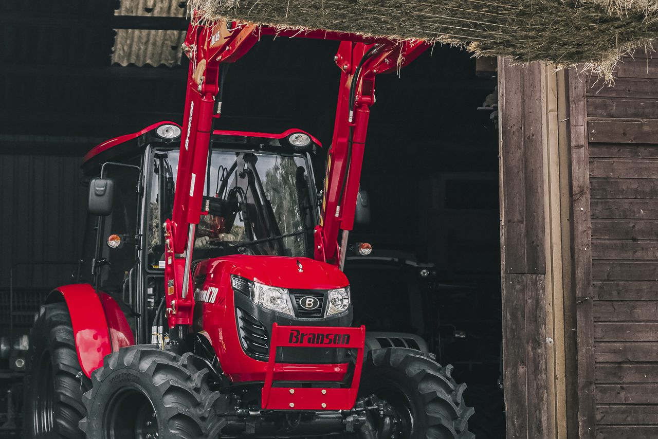 Sicht auf einen roten Branson Traktor der ein Heuballen hebt symbolisch für die Landtechnik